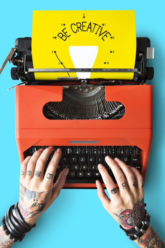 Tatooed hands typing "be creative" in a red typewriter